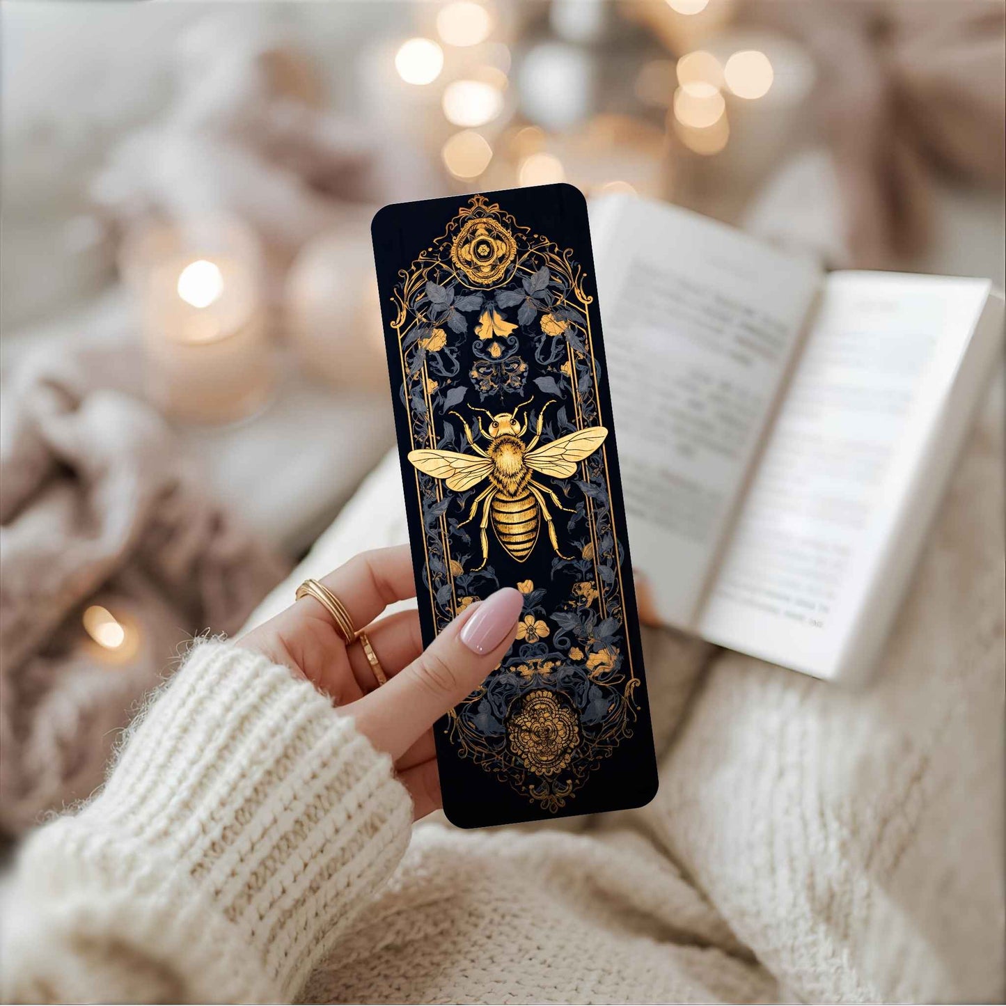 Hand holding a bookmark with a gold bee design against a blurred indoor background