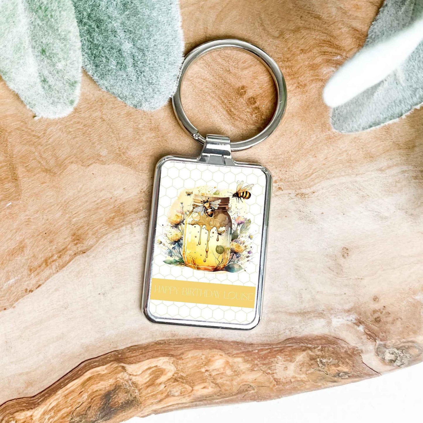 Pretty bee keyring with honeycomb background, silver frame and on a wooden background
