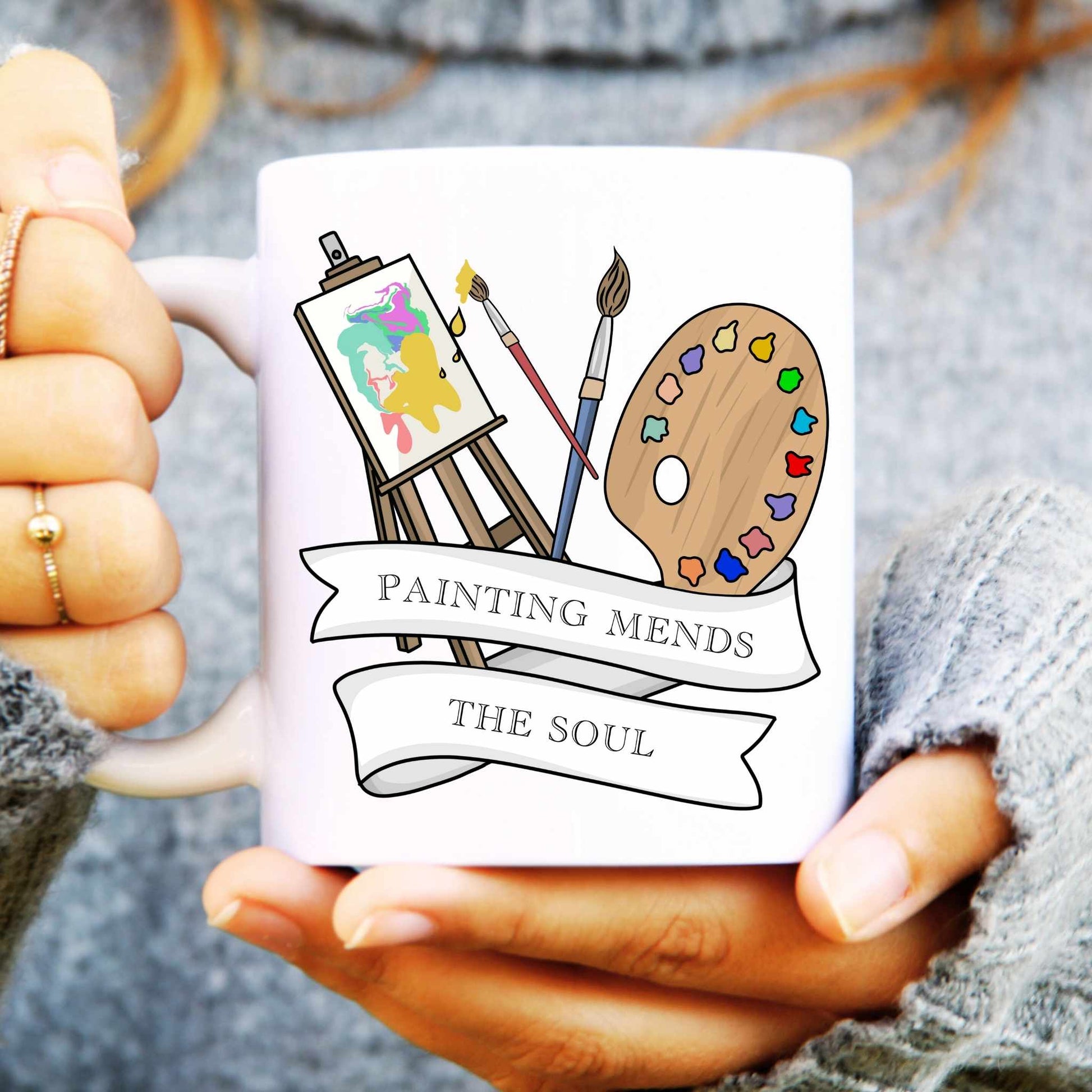 Mug with artistic design and 'Painting Mends The Soul' text held by a person.
