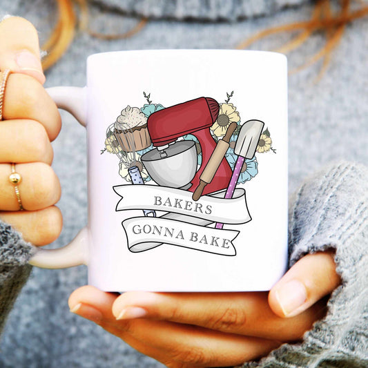 White mug with baking-themed design held by a person wearing a gray sweater.