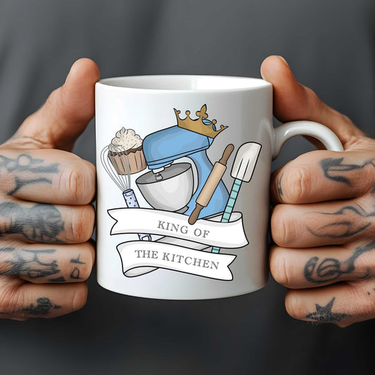 White mug held by hands with tattoos, featuring kitchen-themed design and text 'King of the Kitchen'.