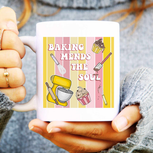 Person holding a mug with baking-themed design and text 'Baking Mends the Soul' on a striped background.