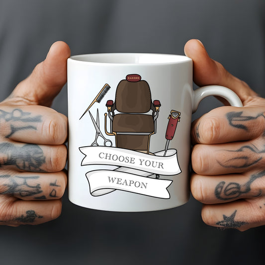 White mug held by tattooed hands with a barber-themed design and 'Choose Your Weapon' text.
