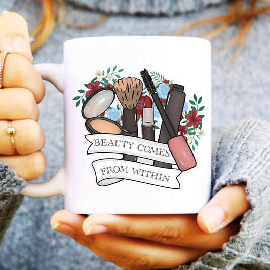 Mug with makeup illustrations and 'Beauty Comes from Within' text held by a person.