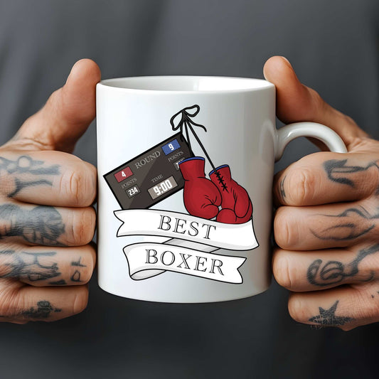 White mug held by tattooed hands with boxing-themed design and text 'Best Boxer'.