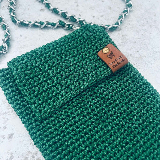 Green crochet phone bag with a leather tag on a light grey background