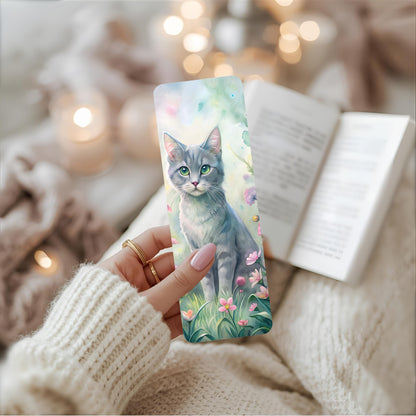 Person holding a bookmark with a cat design, surrounded by soft lighting and cosy background.