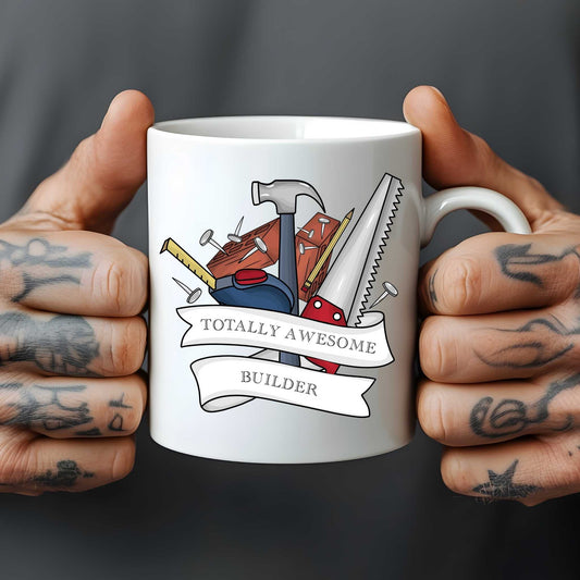 White mug held by hands with tattoos, featuring construction tools and 'Totally Awesome Builder' text.