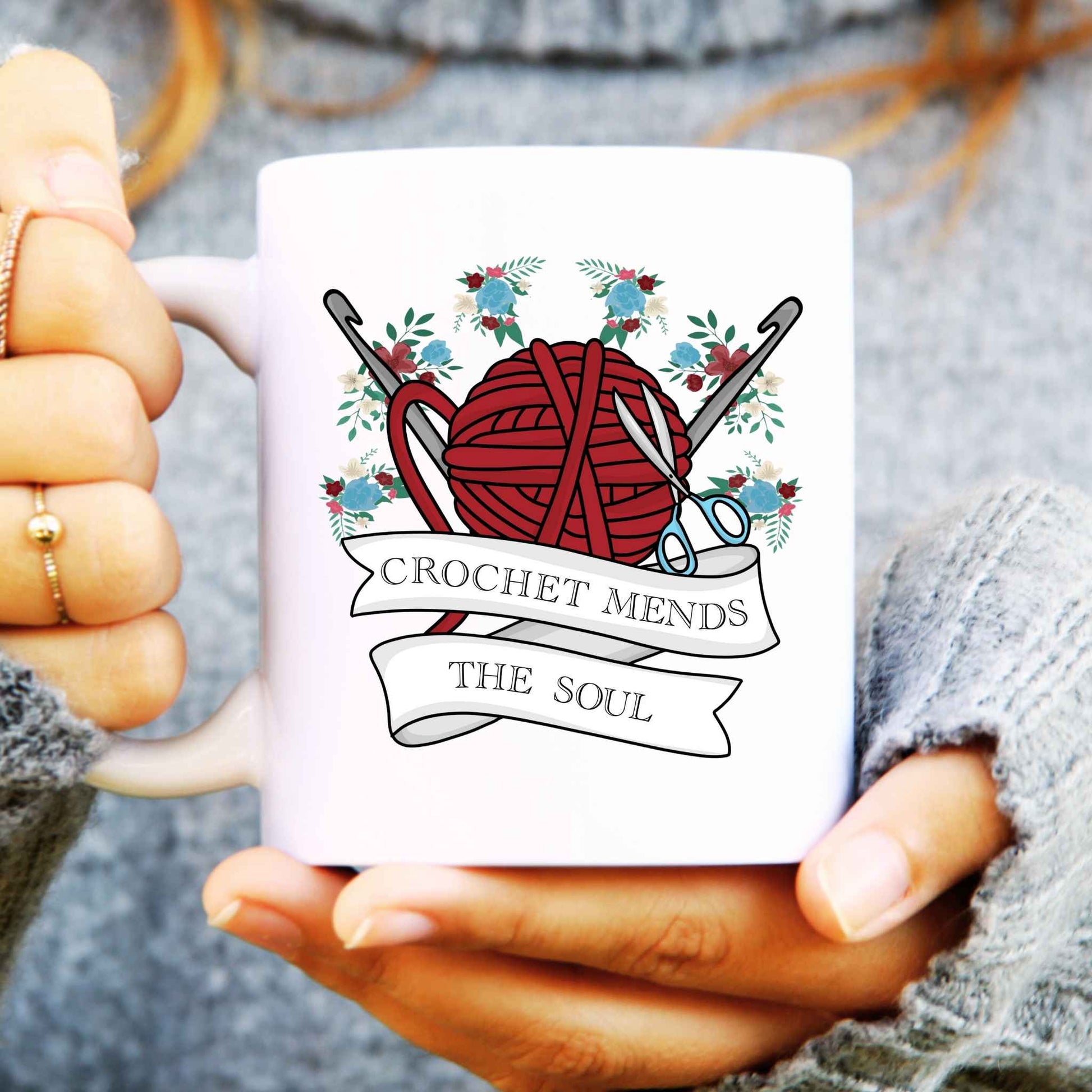 White mug with crochet-themed design held by a person wearing a grey sweater.