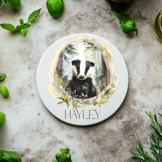 Round coaster with a badger design and the name 'Hayley' on a stone surface with basil leaves.