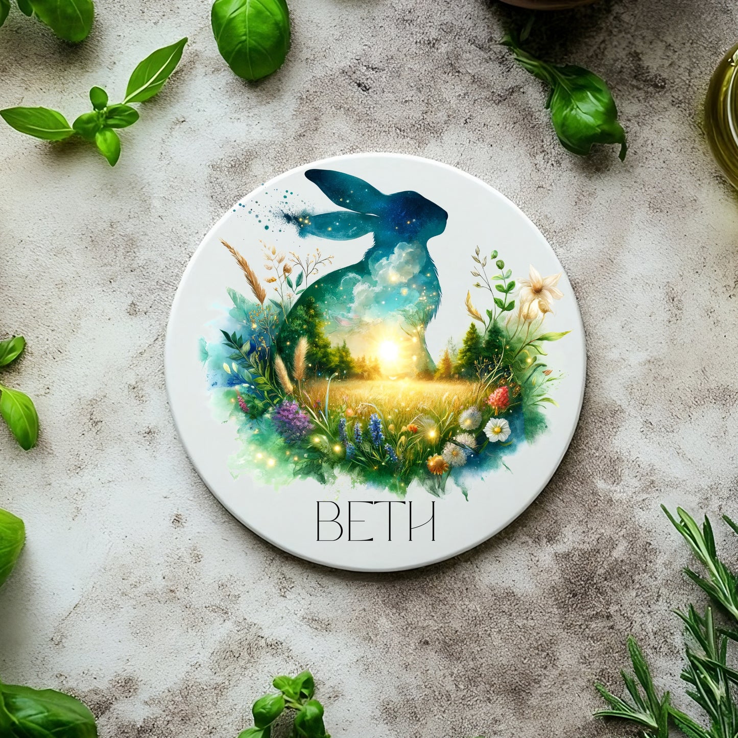 Round coaster with a hare design and 'BETH' text, surrounded by greenery on a textured surface.