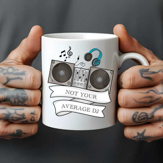 Mug with 'Not Your Average DJ' design held by hands with tattoos on a dark background