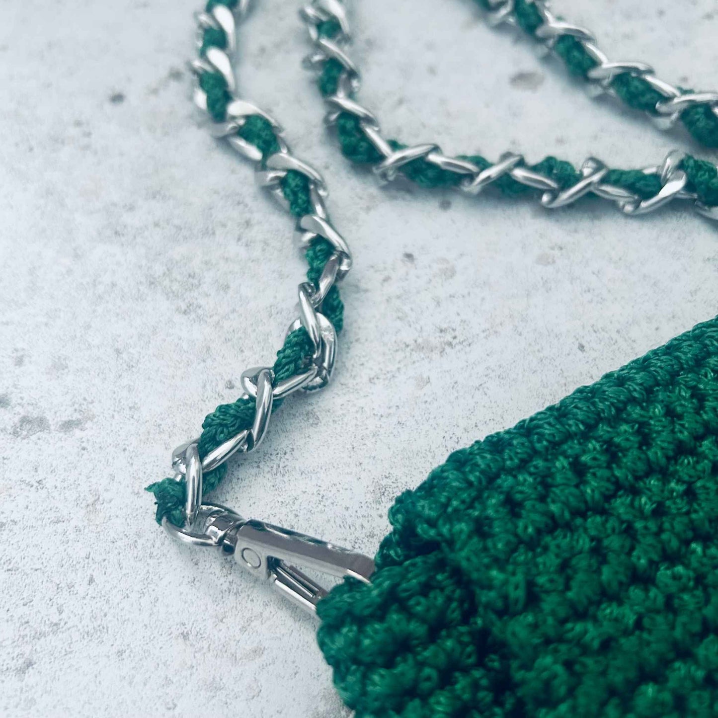 Green crocheted bag with a braided chain strap on a light grey surface