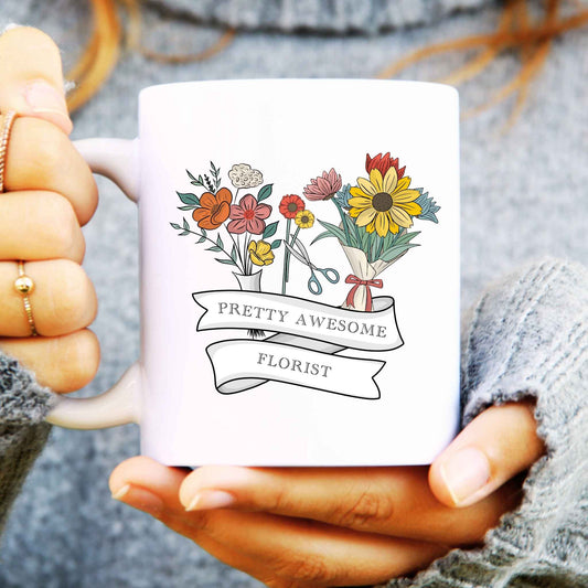 White mug with floral design and 'Pretty Awesome Florist' text held by a person.