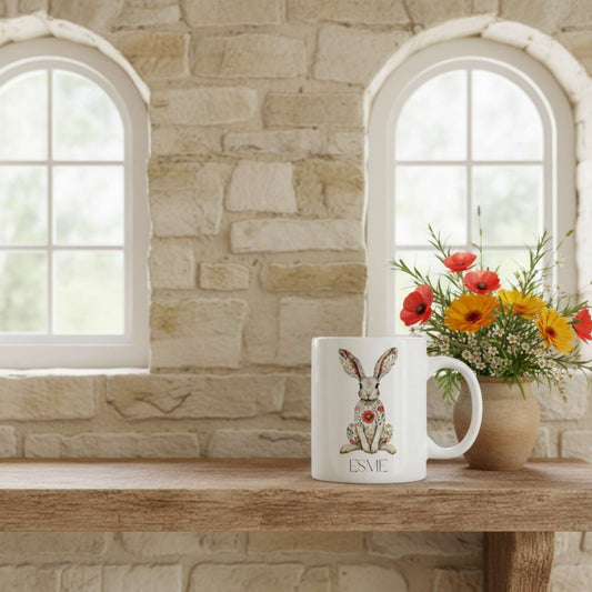 Mug with a hare design and floral patterns on a wooden surface with a stone wall background