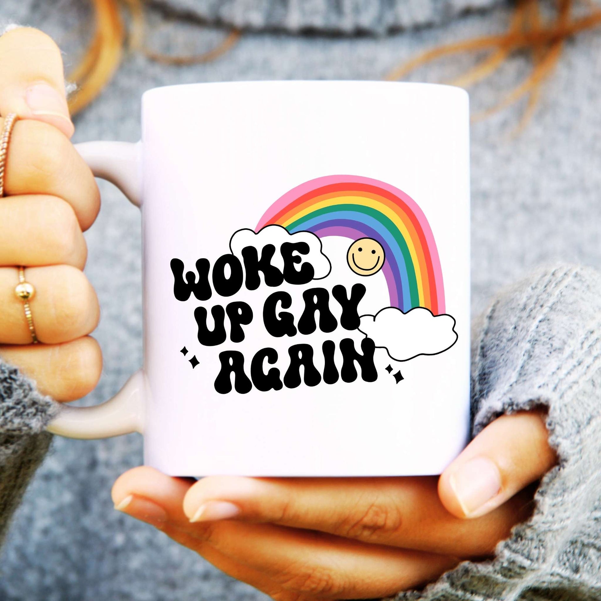 White ceramic mug with a rainbow and smiley face, text reads "Woke Up Gay Again"