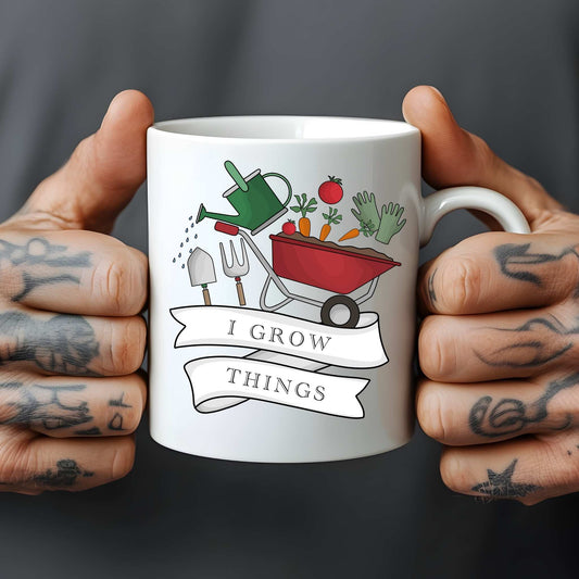 White mug held by tattooed hands with gardening-themed design and 'I Grow Things' text.