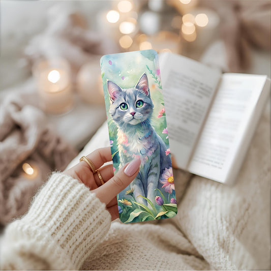 Person holding a bookmark with a cat design, surrounded by soft lighting and cosy background.