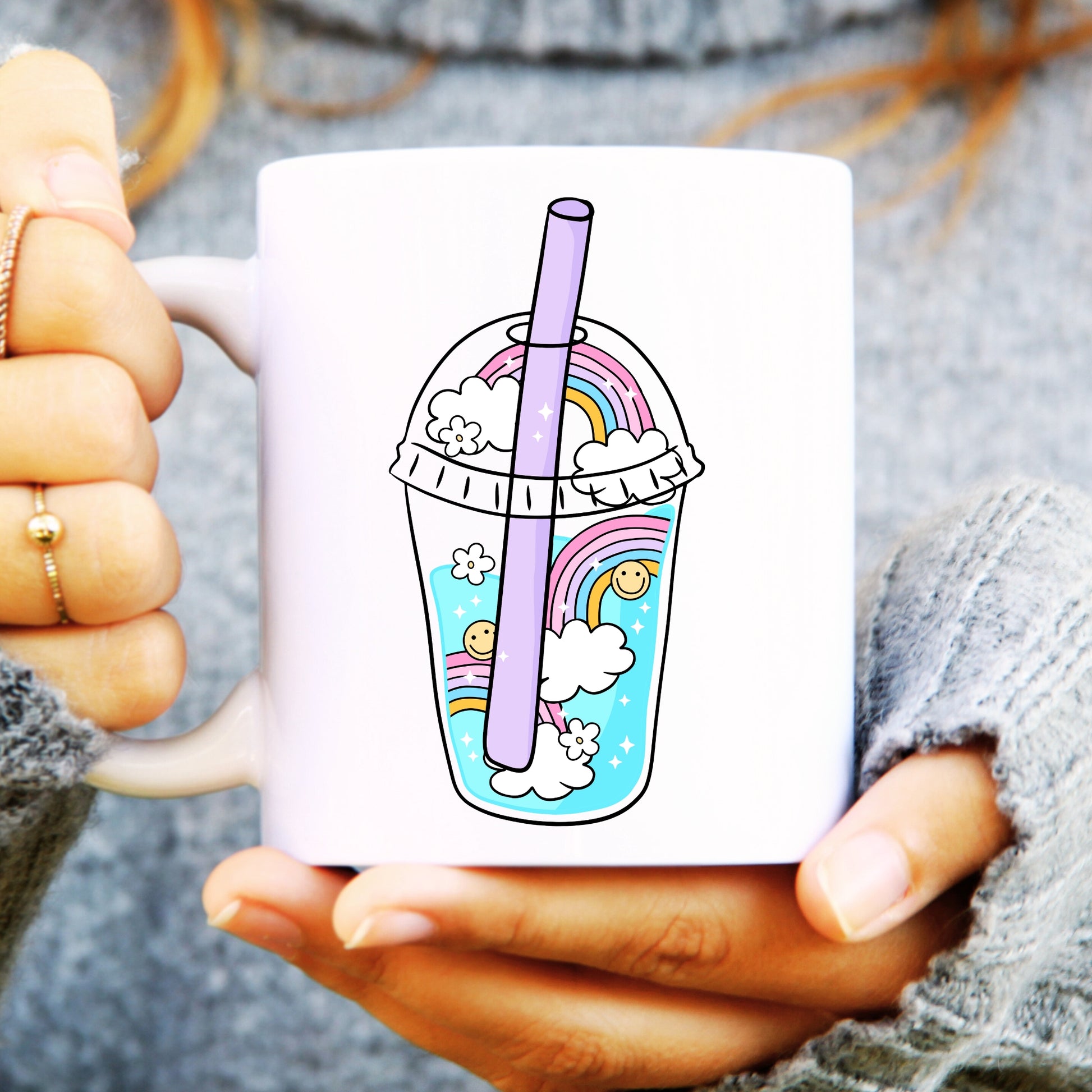 Person holding a white mug with a juice carton with straw and smiley faces and rainbows