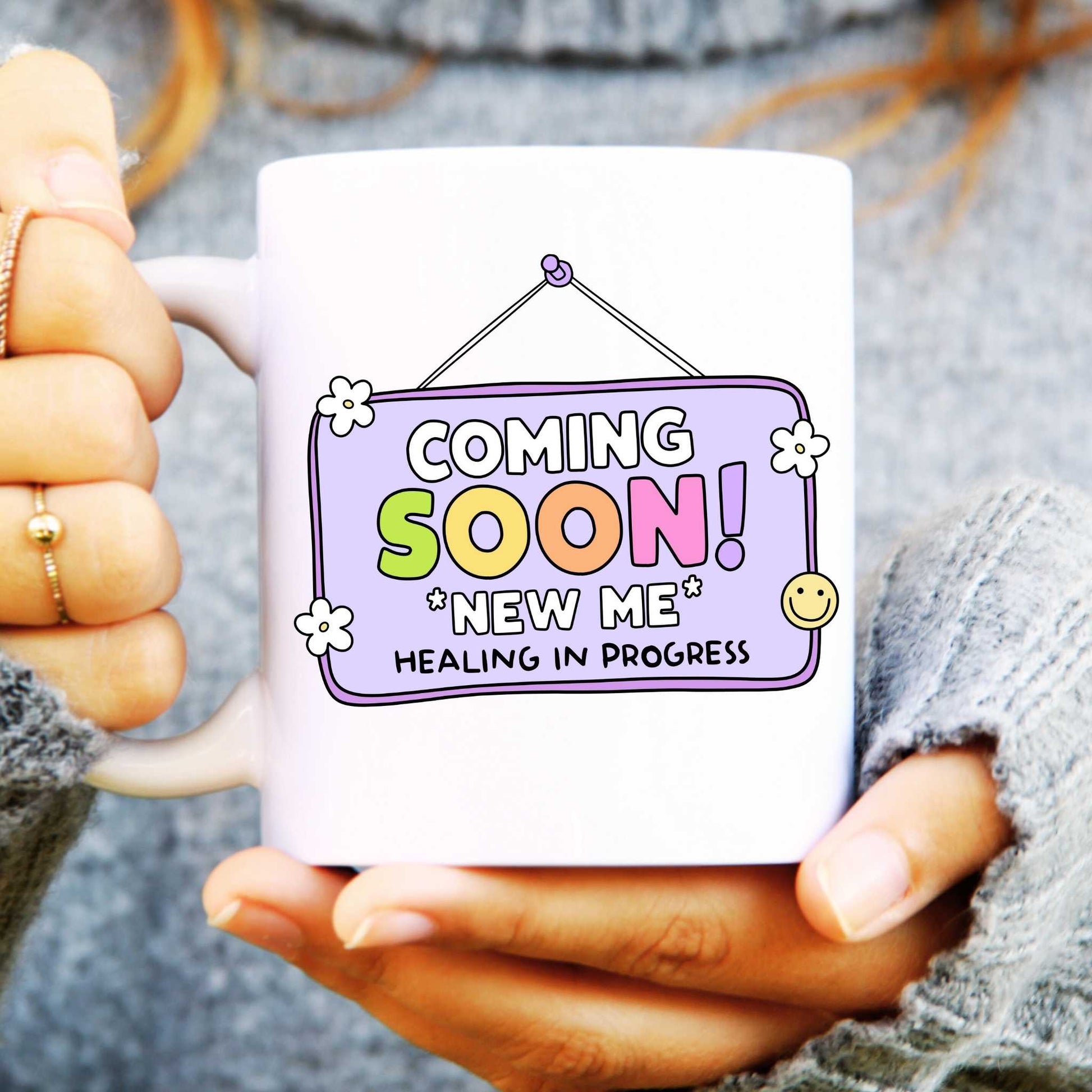 Person holding a mug with 'Coming Soon! New Me Healing In Progress' text