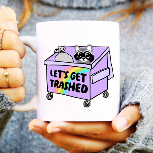 Mug with a raccoon design and 'Let's Get Trashed' text held by hands.