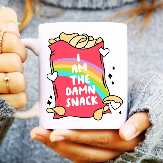 White ceramic mug held in hands with a crisp packet illustration and text reads "I am the damn snack"