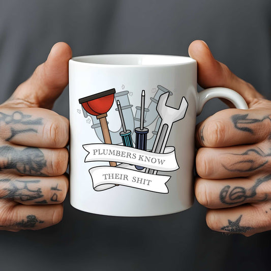 White mug held by tattooed hands with plumbing tools illustration and text.