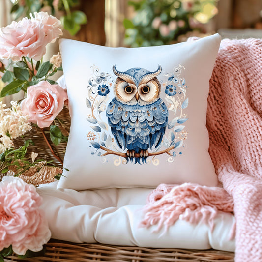 Decorative cushion with an owl design on a surface with flowers and a blanket.