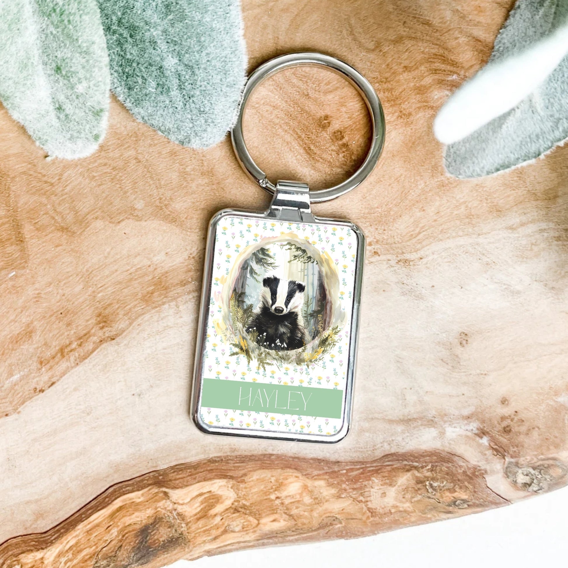 Keychain with a badger illustration and 'Hayley' text on a wooden surface