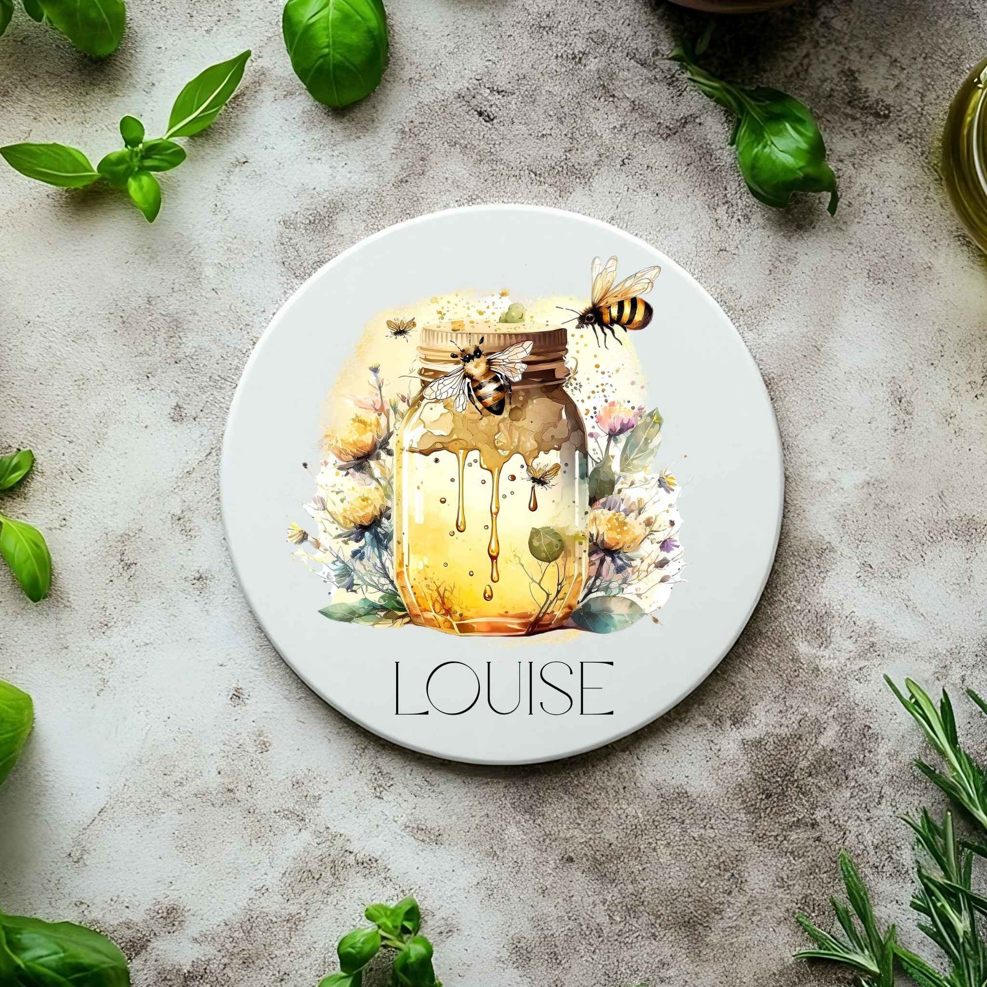 Round coaster with a design of a jar of honey, bees, and flowers on a concrete surface with basil leaves.