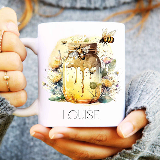 Mug with honey jar and bee design, held by a person wearing a grey sweater.