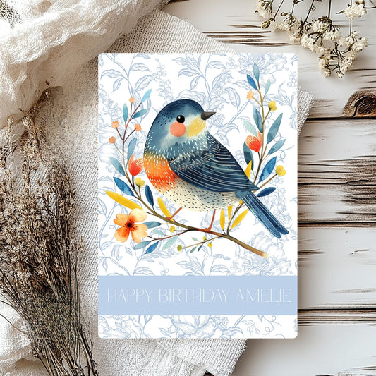 Greeting card with a colourful bird illustration on a floral branch, placed on a textured surface.