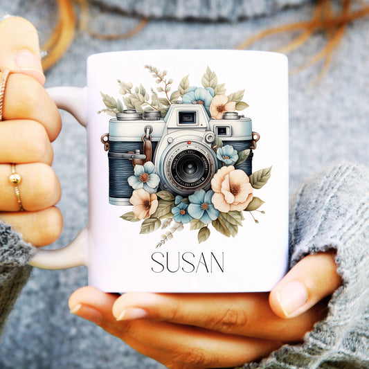 White ceramic mug with pretty camera design surrounded by flowers and personalised with a name.