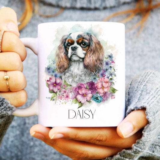 Person holding a mug with a Cavaliar king Charles dog illustration and floral design, labelled 'Daisy'.