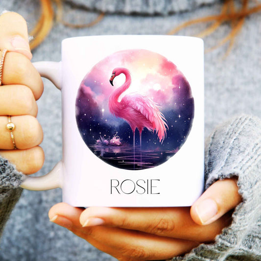 Person holding a mug with a flamingo stood in water and surrounded by night, personalised at the bottom.