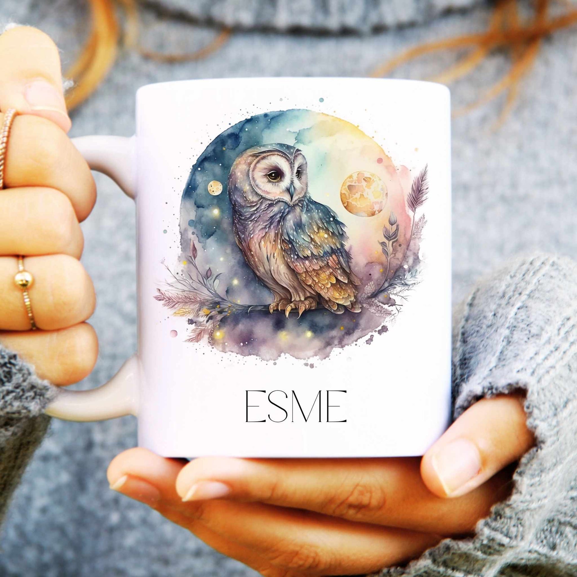 Person holding a mug with an owl design and 'ESME' text