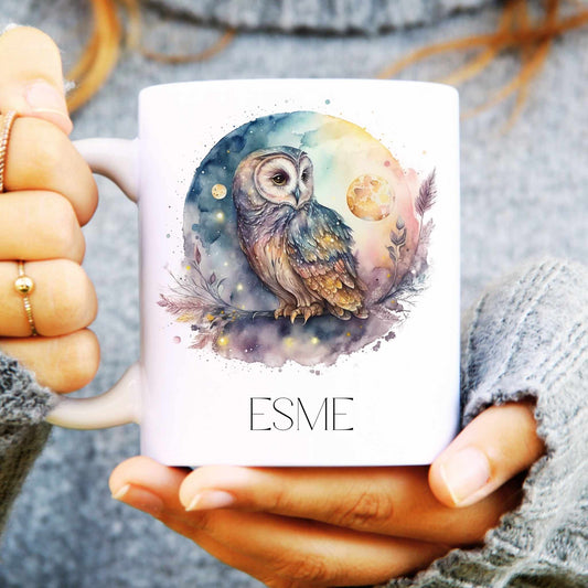 Person holding a mug with an owl design and 'ESME' text