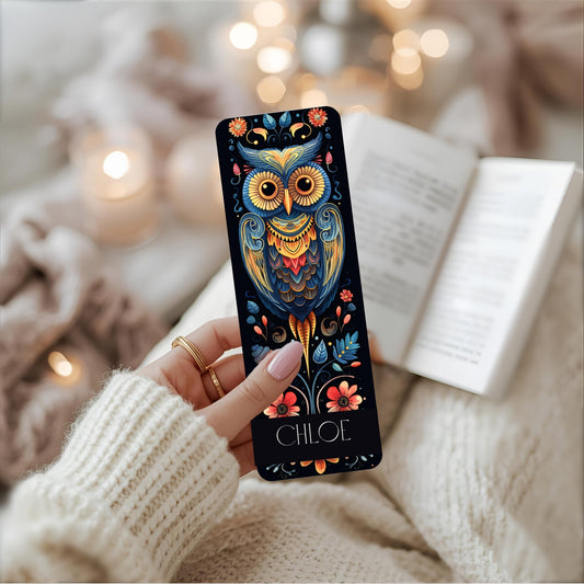 A person presents a book with an owl illustration, showcasing a handcrafted metal bookmark ideal for readers and owl fans.