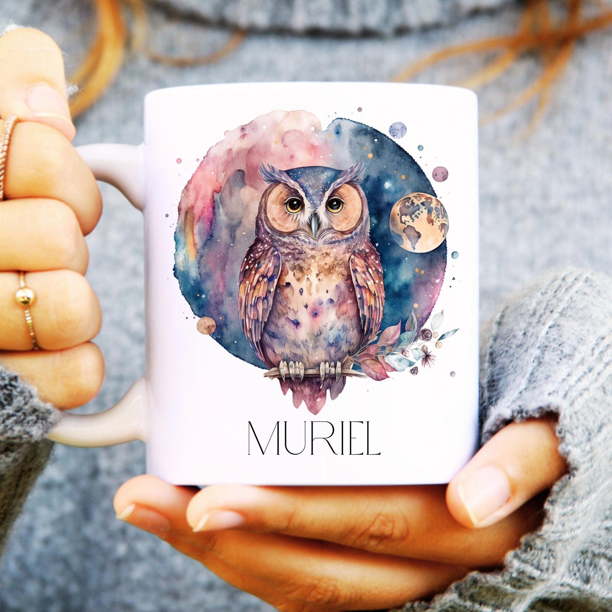 Person holding a mug with an owl design and 'Muriel' text