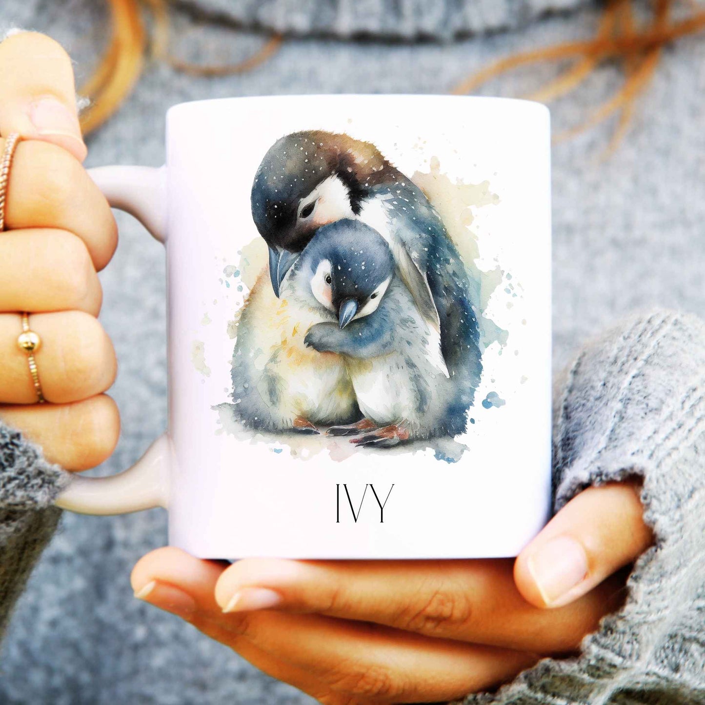 Watercolour penguins on a white ceramic mug personalised and held in someone's hands.