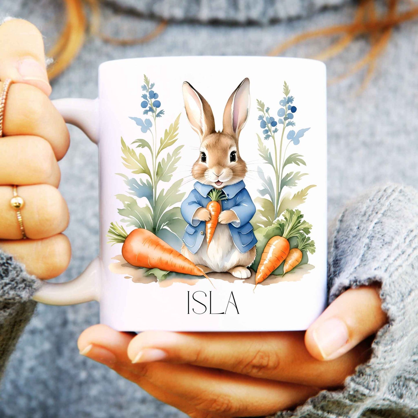 Person holding a mug with a rabbit and carrot design, featuring the name 'ISLA'.