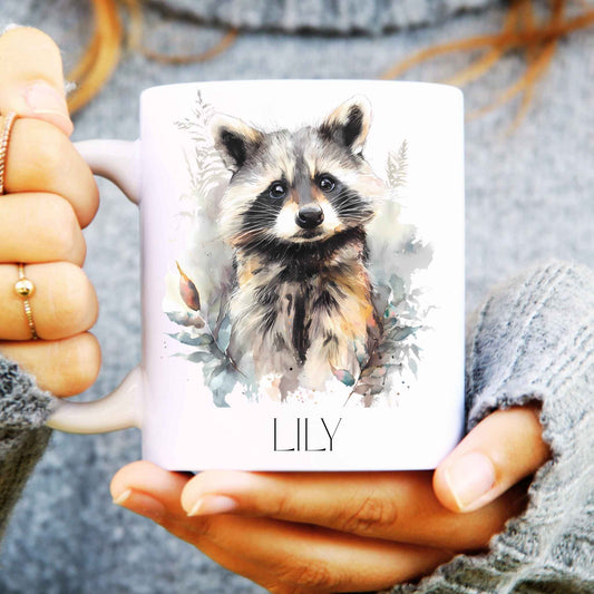 Person holding a mug with watercolour raccoon and personalised with a name at the bottom.