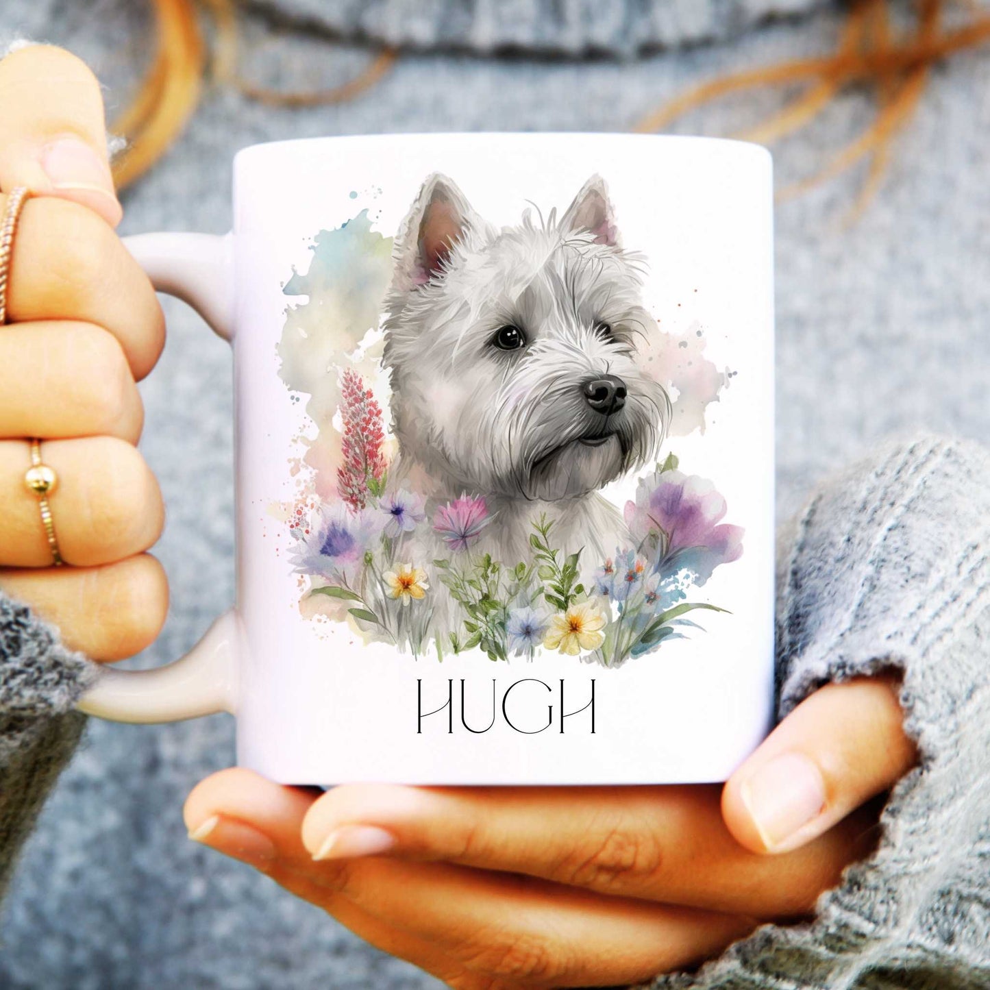 Person holding a mug with a west highland terrier dog illustration and the name 'Hugh' on it.