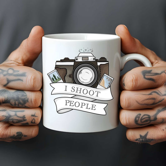 White mug held by tattooed hands with a camera design and 'I Shoot People' text relating to photography.