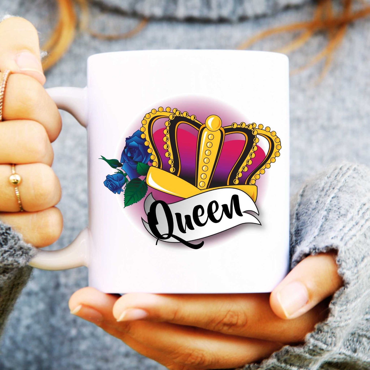 White mug with 'Queen' design held by a person wearing a grey sweater.