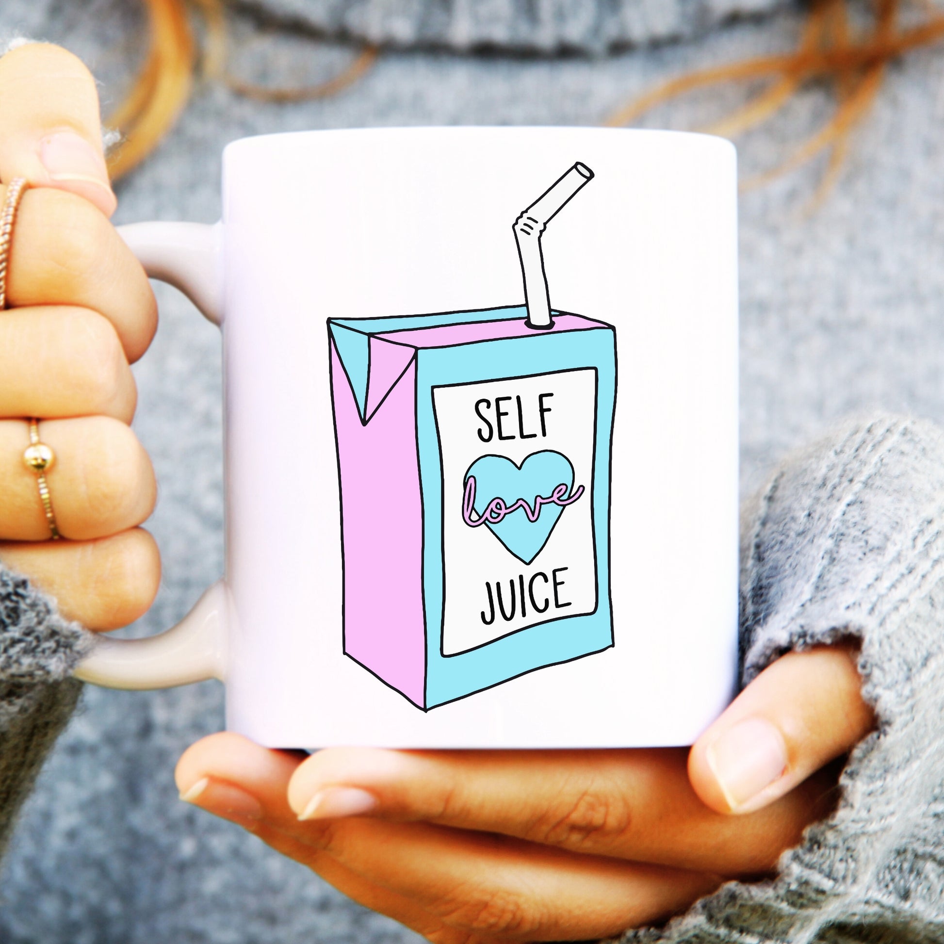 Woman holding a ceramic white mug with a carton on the front saying self love juice.