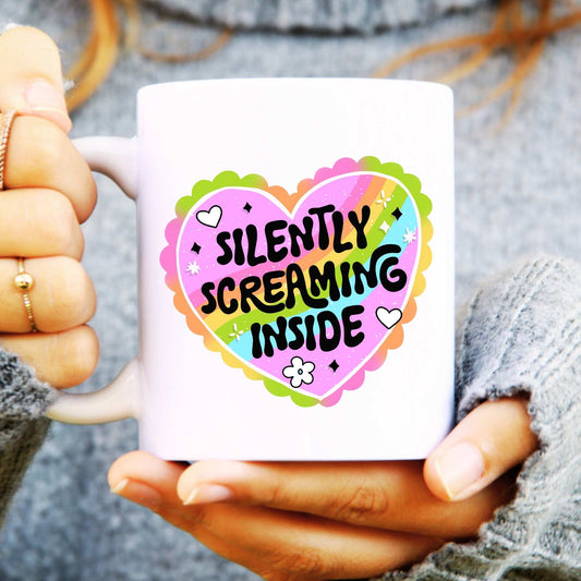Mug with colourful heart design and text  reads "Silently Screaming Inside" held by a person
