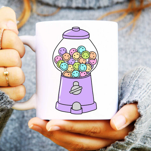 White mug with a colourful gumball machine design held by a person.