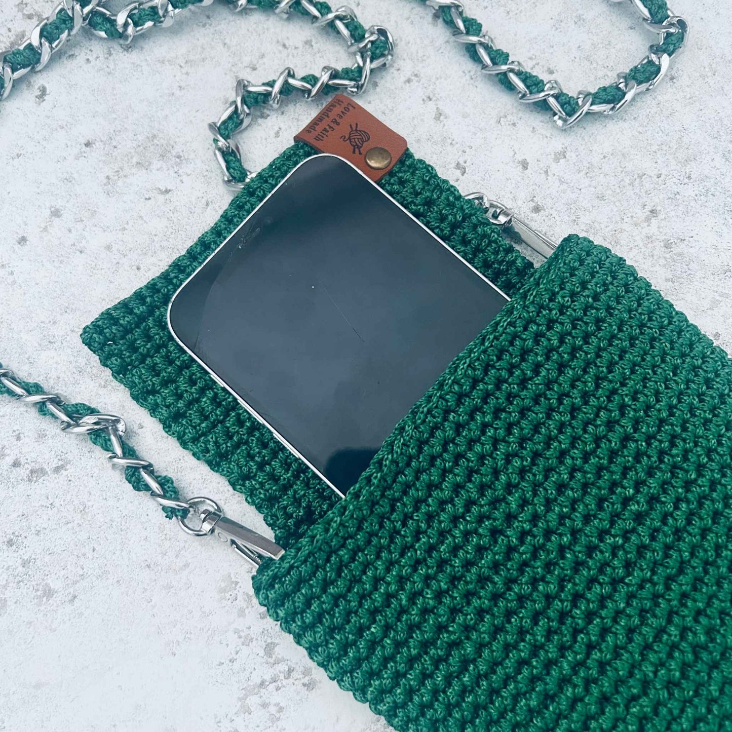 Green knitted phone pouch with chain strap on a light grey background