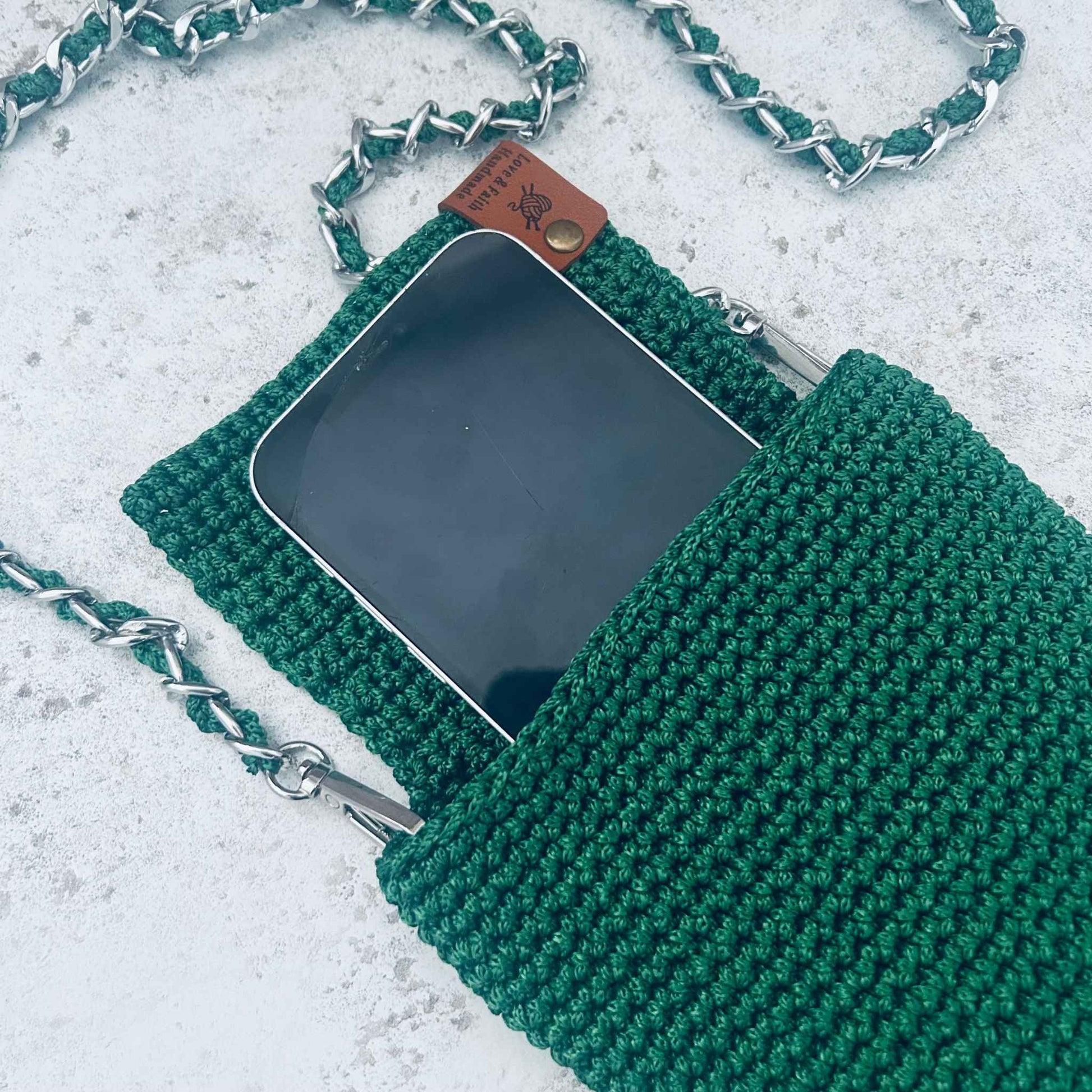 Green knitted phone pouch with chain strap on a light grey background